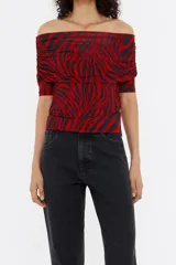 Camiseta ajustada con estampado de cebra en rojo y negro. Presenta escote recto con vuelta que permite usarla estilo off-shoulder, y mangas tres cuartos ajustadas.
