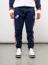Pantalon de jogging azul marino de felpa, con franjas laterales en rojo y blanco. Presenta el escudo del Club Nacional de Football bordado en el muslo derecho y el logo de Umbro en el izquierdo.