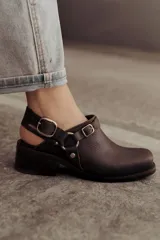Zueco de cuero marrón oscuro, con diseño cerrado en la parte delantera, tira ajustable en el talón con hebilla metálica y taco bajo cuadrado.