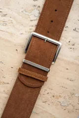 Cinto marrón de gamuza con hebilla metálica plateada.