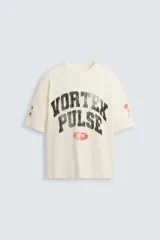 Camiseta de manga corta color crema, corte boxy fit, con cuello redondo. Presenta un estampado frontal en negro con el texto 'VORTEX PULSE' y el número '1974' en un óvalo rojo desgastado. Tiene pequeños detalles gráficos rojos en las mangas.