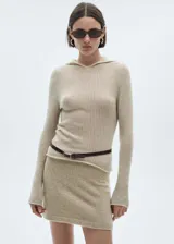 Jersey de punto acanalado en color beige, con diseño de manga larga y capucha integrada. Presenta un corte ajustado y acabado con bordes sin costuras visibles.