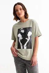 Remera de algodón color verde oliva con cuello redondo y mangas cortas con dobladillo. Presenta una estampa fotográfica central en blanco y negro de estilo editorial.