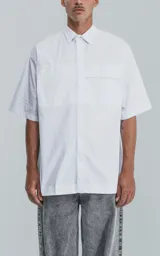 Camisa de manga corta en popelina de algodón, con silueta oversize y diseño funcional que incluye dos bolsillos delanteros, uno de ellos con solapa.