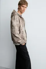 Cazadora negra de algodón con efecto lavado, corte relajado y capucha ajustable. Presenta cierre frontal de cremallera, bolsillos frontales tipo canguro y elásticos en puños y bajo.