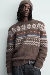 Jersey de punto con textura, corte relajado, cuello redondo y manga larga. Presenta un diseño jacquard geométrico con motivos de copos de nieve en tonos marrones, azules y blancos.