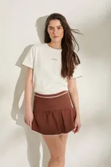 Minifalda tejida de punto en color marrón, de corte ajustado en la cintura con volado fruncido en el bajo y detalles de costuras blancas a contratono en la cintura y el ruedo.