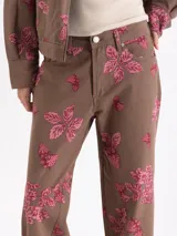 Pantalon de corte recto y tiro medio, confeccionado en tela color marrón con estampado de fresas y hojas en tono rosado. Cuenta con cierre frontal y bolsillos laterales.