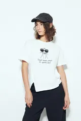 Remera blanca de manga corta con estampa frontal de un personaje con lentes de sol y la frase "Llegué tarde porque no quería venir". Tiene silueta relajada y calce cómodo, con un corte asimétrico en el bajo.