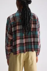 Camisa de algodón con estampado de cuadros estilo tartán en tonos marrón, turquesa y rosado. Presenta un calce relajado y largo cropped, cuello clásico, hombros caídos, bolsillo aplicado en el frente y mangas amplias con puños ajustados. El ruedo cuenta con terminación desflecada.