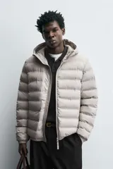 Campera puffer acolchada de corte regular fit en color negro, confeccionada en tejido técnico repelente al agua. Presenta cuello subido con capucha, cierre frontal de cremallera, mangas largas con puños elásticos y bolsillos laterales de vivo.