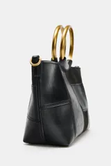 Bolso tipo saca en formato mini con diseño de patchwork en tonos marrones. Cuenta con una anilla metálica rígida como asa de mano y una correa bandolera extraíble. El cierre principal es mediante imán e incluye un bolsillo interior con cremallera.