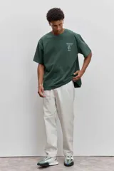 Remera de algodón color verde oscuro, de corte holgado y manga corta, con pequeño estampado gráfico en el pecho.