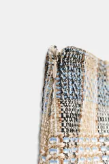 Falda pantalón de tiro alto confeccionada en tejido de tweed con estampado a cuadros en tonos beige, azul y negro. Presenta detalles de falsos botones y cierre lateral con cremallera oculta.