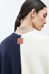 Ruana de tejido de punto con diseño color block en tonos crudo, gris y negro, con terminación de flecos en el ruedo y textura en relieve.