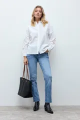 Camisa blanca de corte recto con cuello clásico y cierre frontal de botones. Presenta mangas largas con detalles de encaje calado en los antebrazos y puños abotonados.