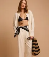 Pantalón recto de cintura alta confeccionado en viscolino color crudo, con elástico en la parte trasera de la cintura, cierre tradicional y textura de palmeras perforadas en el bajo.