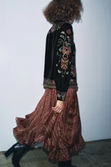 Chaqueta de terciopelo negro con cuello solapa y manga larga. Presenta un diseño con bordados florales y geométricos a contraste en tonos tierra y ocres. Cuenta con cierre frontal de botones y forro interior.
