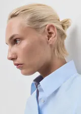 Camisa de corte entallado confeccionada en popelín de algodón con elastano. Presenta cuello camisero clásico, cierre frontal con botones y mangas largas con puños abotonados.