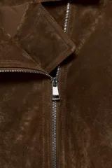 Cazadora corta de ante color marrón, con cuello de solapa, cierre frontal cruzado con cremallera, mangas largas con cremalleras en los puños y bajo con cinturón ajustable.