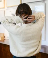 Sweater de lana merino color marfil, tejido a mano, con cuello redondo y detalles de punto trenzado y calados en V en el frente y las mangas.