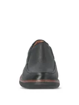 Zapato tipo mocasín Hush Puppies modelo Oregon, confeccionado en cuero negro con textura granulada. Presenta un diseño slip-on con elásticos laterales, costuras reforzadas y una suela de goma EVA que proporciona flexibilidad y aislamiento térmico.