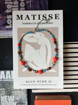 Collar corto de cuentas multicolor que combina cuentas esféricas de piedra jaspe dálmata, cuentas turquesas, cuentas naranjas brillantes, cuentas marrones y abalorios translúcidos, con cadena de ajuste y cierre de mosquetón plateado.