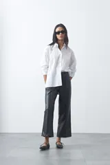Pantalón de corte recto y pierna ancha confeccionado en cuero sintético negro, con acabado estructurado y tiro medio.