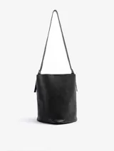 Cartera bandolera de cuero floater color negro, de diseño cilíndrico tipo bucket, con correa larga para llevar al hombro o cruzada y broche de imán.