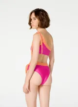 Bikini de dos piezas marca Blueman, con corpiño asimétrico de un solo hombro y bombacha de tiro alto con lazos laterales. Diseño color fucsia con detalles en naranja.