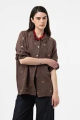 Camisa de lino color chocolate, de corte relajado y mangas largas con detalles bordados florales en contraste. Cuenta con cuello clásico y cierre frontal de botones.