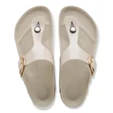 Sandalias tipo ojota Birkenstock modelo Gizeh, color beige con hebilla grande dorada y suela de corcho con base de goma negra.