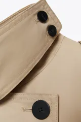 Trench color beige con cuello solapa y manga larga ajustable con trabillas. Bolsillos en delantero. Cinturón en mismo tejido. Detalle de pespuntes marcados a tono. Cierre frontal cruzado con botones. Tejido repelente al agua.