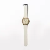 Reloj de pulsera con caja dorada, esfera color crema con agujas doradas y correa de silicona blanca con textura.