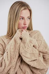 Buzo de tejido de punto grueso en color negro, con cuello alto y diseño de trenzas y relieves en toda la prenda. Presenta mangas largas con terminación ajustada y corte holgado.