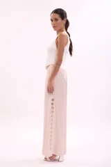Pantalón largo de tiro alto, color rosa pálido, de corte ancho y fluido. Presenta una hilera de recortes ovalados decorativos a lo largo de la costura lateral.