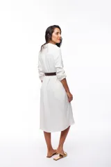 Vestido camisero blanco de poliéster con corte midi, cuello camisero, mangas largas con puños abotonados, cierre frontal con botones y cinturón marrón.