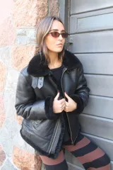 Campera tipo bomber de cuero genuino color negro, con interior y cuello de piel sintética negra. Presenta cierre frontal, detalles de hebillas en el cuello y diseño clásico de aviador.