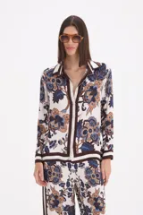 Camisa de manga larga con cuello clásico y cierre frontal de botones. Presenta un estampado floral en tonos beige, marrón y azul, con detalles de bordes en color marrón oscuro.