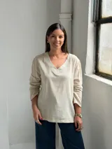 Blusa de lino color beige con escote en V, mangas largas con sutiles frunces en los hombros y costuras decorativas visibles en el cuello y el ruedo.