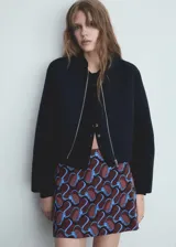 Chaqueta tipo bomber de color negro con cuello redondo y cierre frontal con cremallera metálica. Presenta un diseño recto de manga larga y cuenta con forro interior.