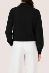 Abrigo de punto color negro, con cuello camisero, cierre frontal completo y dos bolsillos frontales tipo parche. Posee puños acanalados y diseño de corte recto.