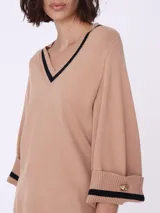 Sweater color beige de tejido de punto, con escote en V con borde negro y mangas 3/4 con puños con detalle de botón dorado.