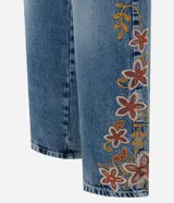 Pantalón wide leg de jean azul con bordado floral aplicado en los laterales. Posee cintura mediana con trabillas, cierre frontal con botón y cremallera, y bolsillos funcionales.