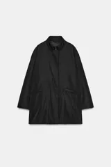 Chaqueta oversize de nylon en color negro, con cuello redondo subido, manga larga y cierre frontal con botones a presión ocultos. Presenta bolsillos delanteros y forro interior a tono.