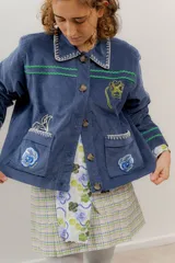 Chaqueta de pana terciopelo azul con bordados a mano y a máquina, con cuello clásico, cierre frontal con botones y bolsillos delanteros.