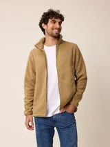 Campera de sherpa color tostado, con cuello alto, cierre frontal completo y bolsillos laterales. Presenta un pequeño logo bordado en el pecho.