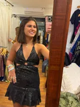 Vestido corto negro con lentejuelas, escote pronunciado en V con argolla central, cut-outs laterales bajo el busto y falda con volado.