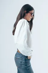 Camisa blanca de manga larga con diseño de rayas verticales sutiles en la misma tela. Presenta cuello clásico, cierre frontal con botones y mangas abullonadas con puños elásticos.