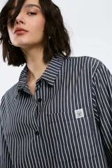 Camisa popelina rayada color rojo y blanco, con corte oversized, abotonadura frontal y en las mangas, y un bolsillo frontal.
